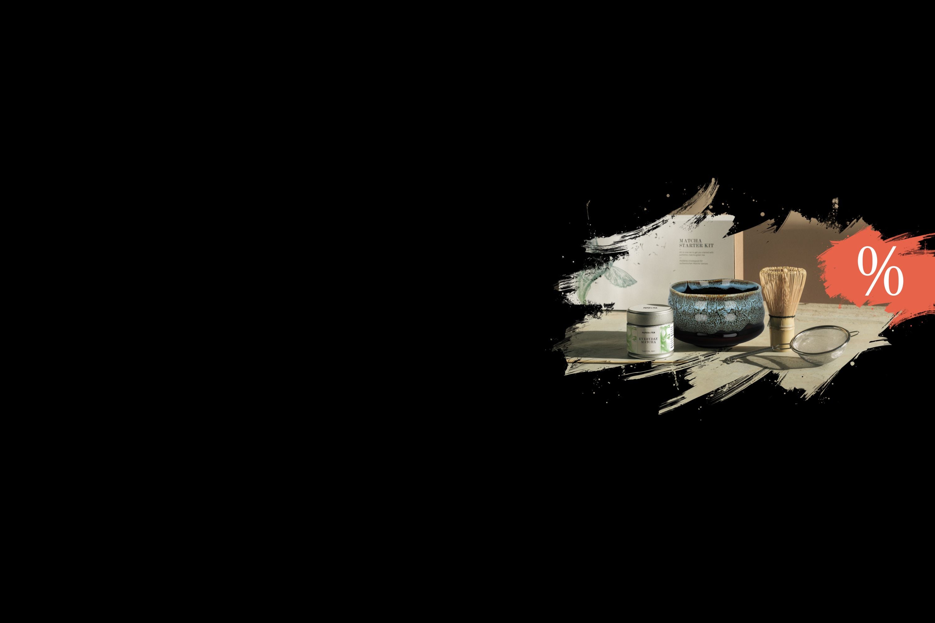 Minimalistisch arrangiertes Matcha-Set mit Matcha-Dose, blauer Schale, Bambusbesen und Sieb auf schwarzem Hintergrund