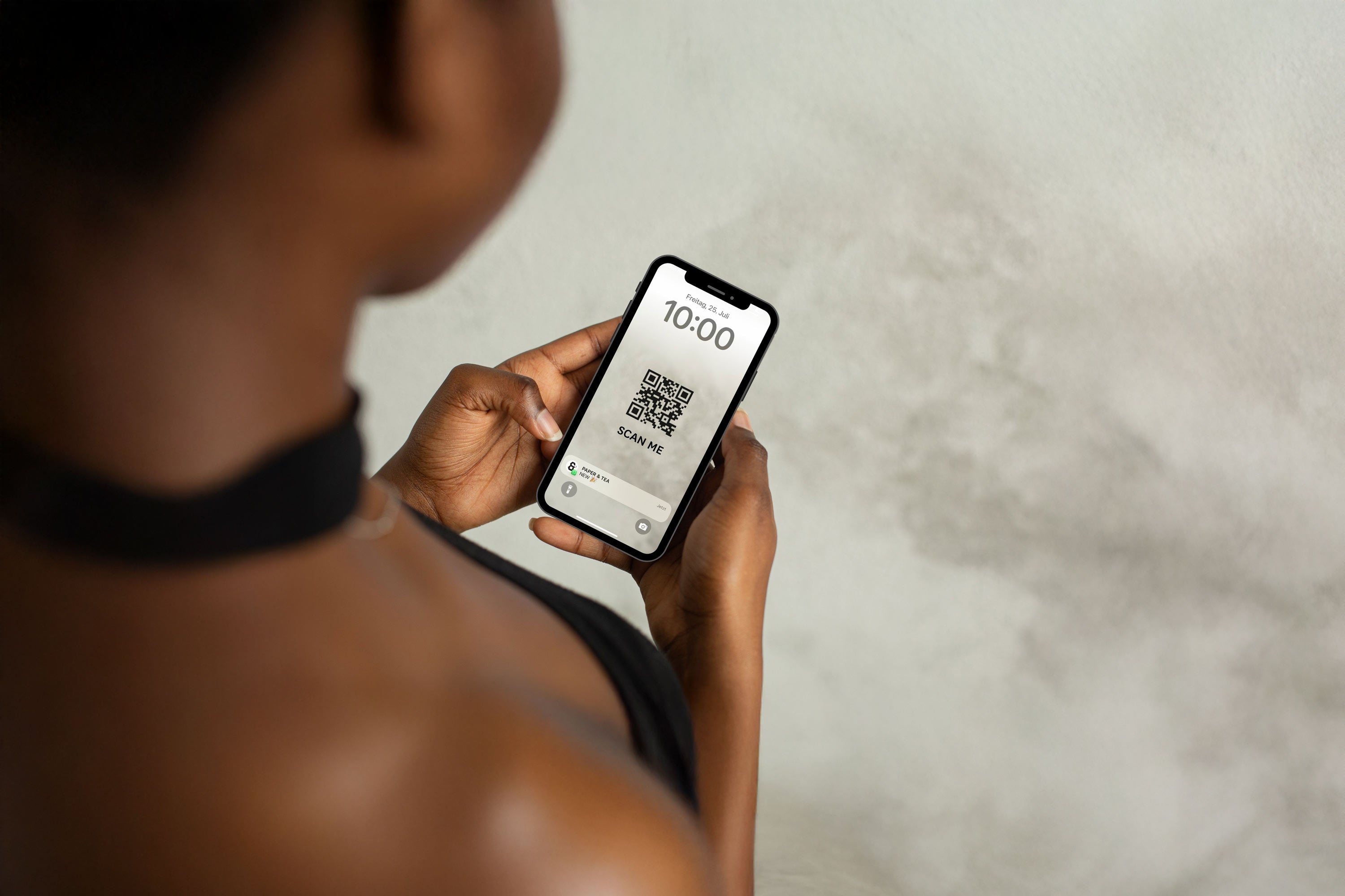 Person hält Smartphone, zeigt QR-Code und Paper & Tea-Benachrichtigung auf weißem Bildschirm.