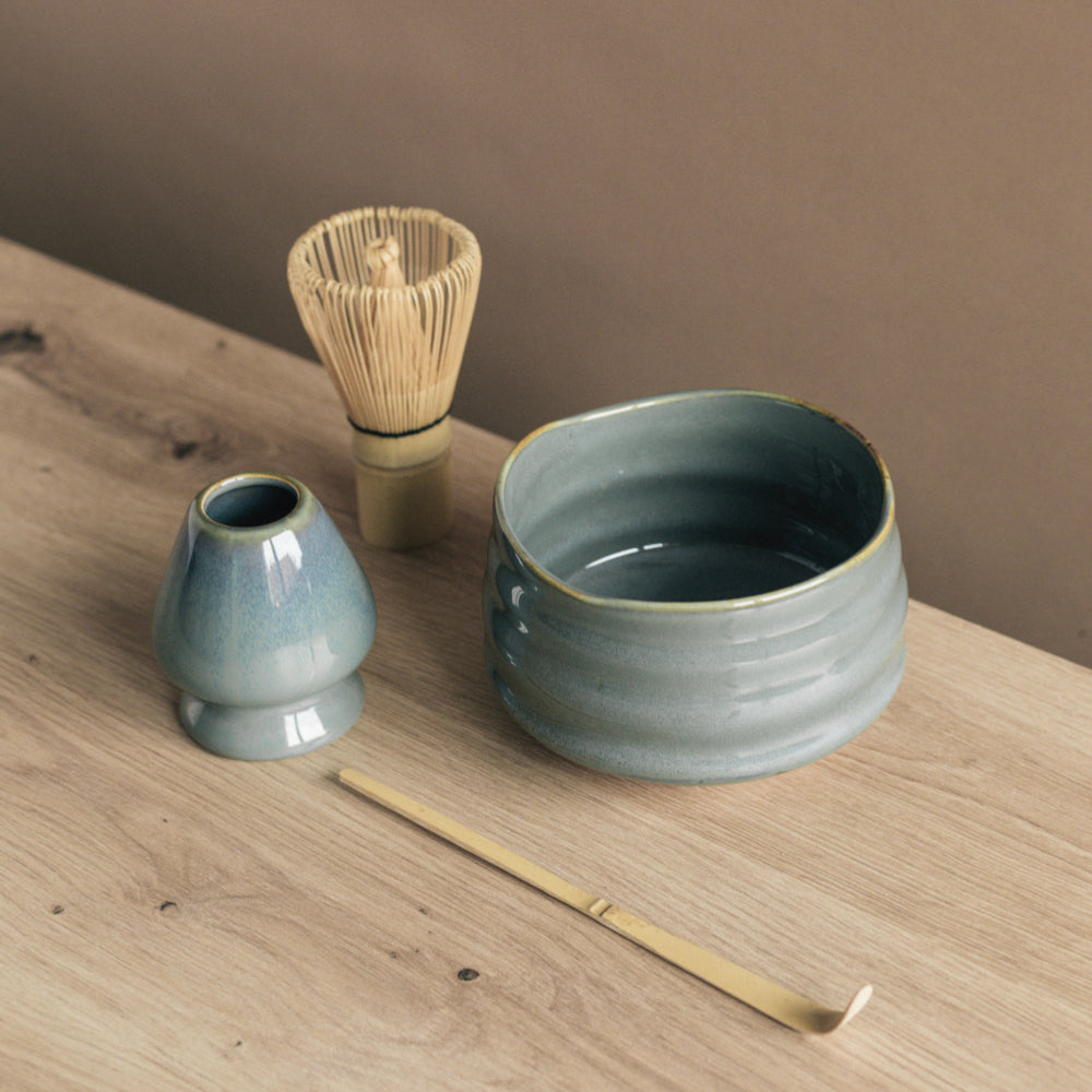 Japanisches Matcha-Teeservice mit Keramikschalen und Bambus-Teewerkzeugen auf hellem Holztisch.