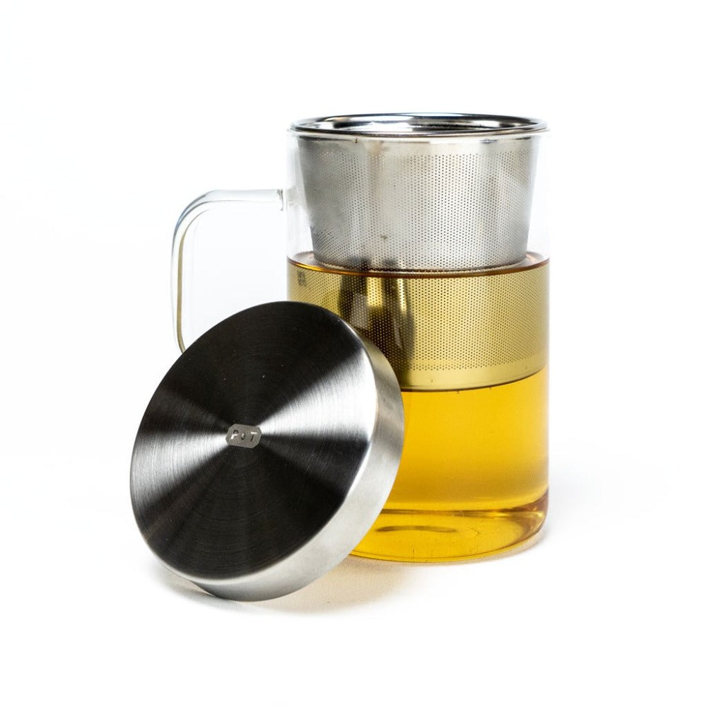 Klare Teetasse mit gelbem Tee, Edelstahl-Teesieb und passender Teedeckelplatte aus gebürstetem Edelstahl.