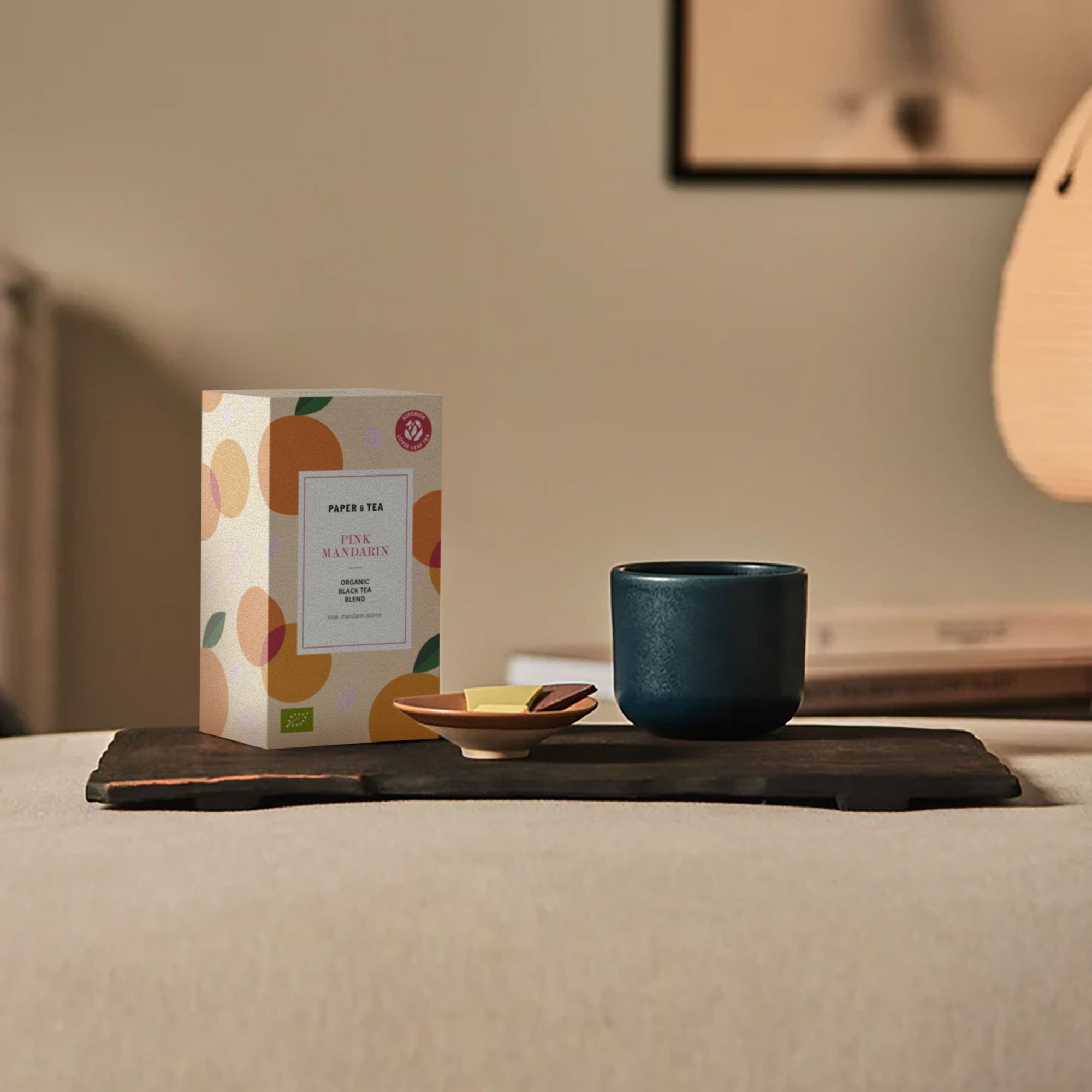 Packung PINK MANDARIN Bio-Schwarztee auf Tablett mit Keramiktasse und Schokoladenstücken