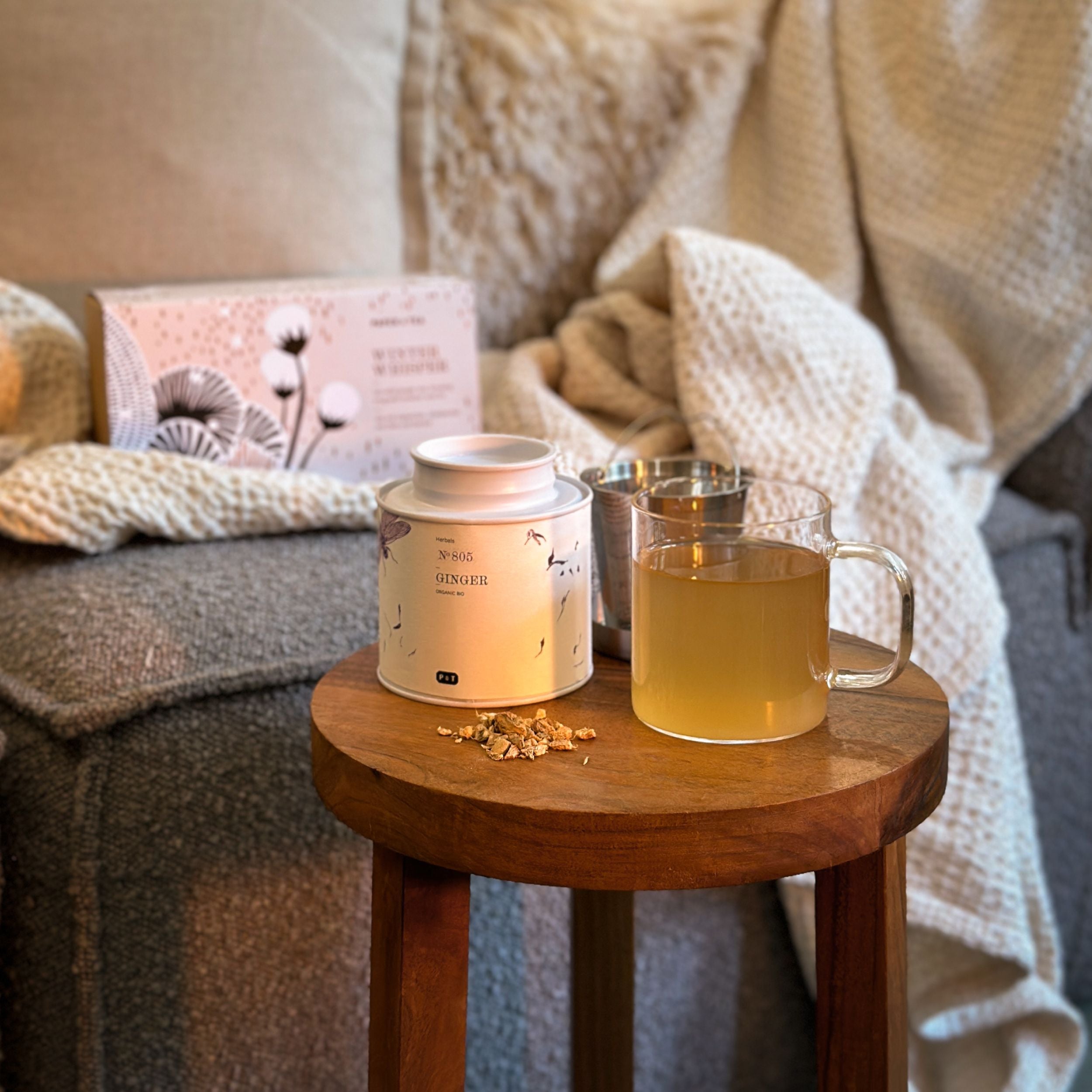 Weiße Dose mit Bio-Ingwertee von P & T, Glas mit warmem Ingwertee, getrocknete Ingwerstücke auf Holzschemel.