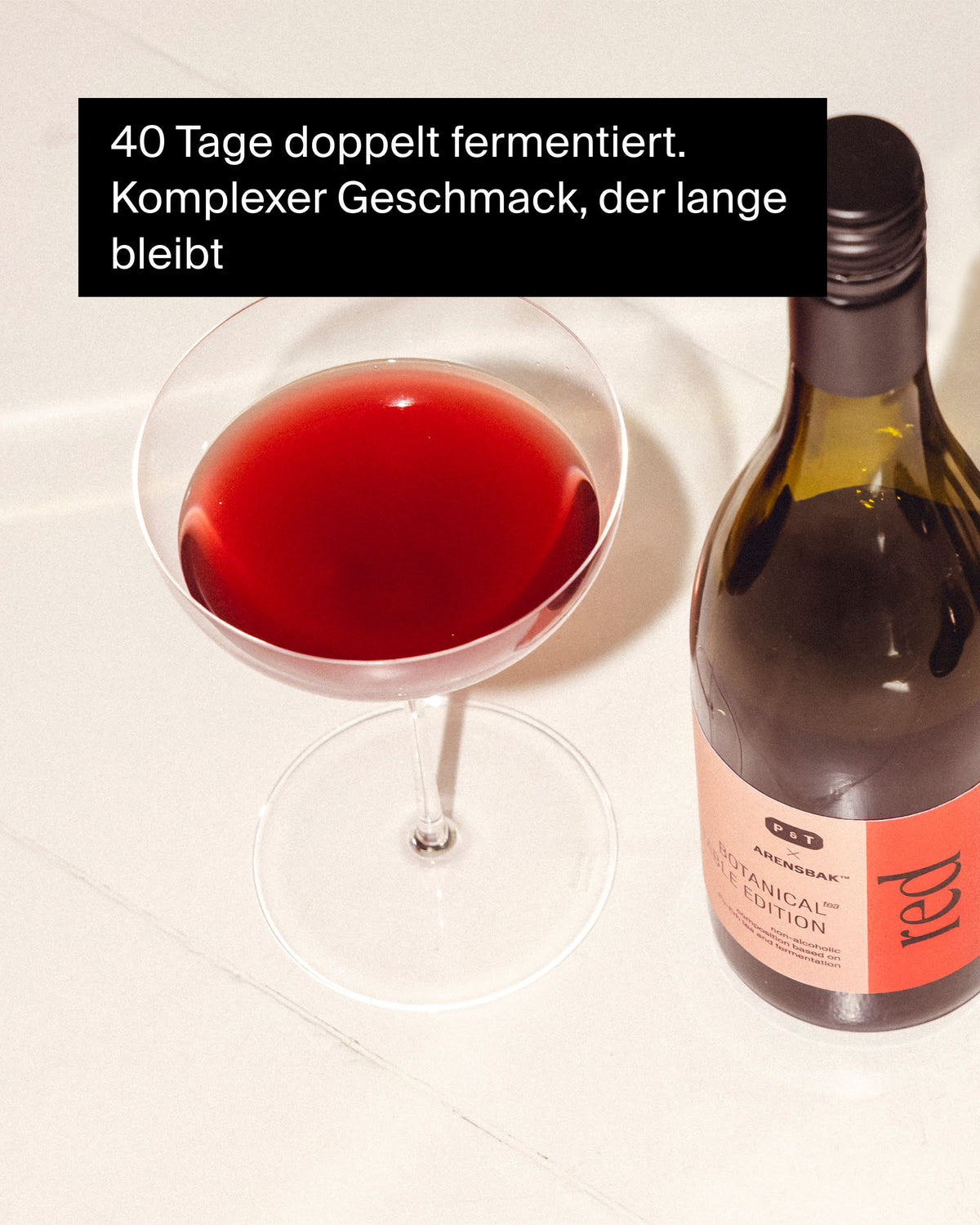 Klares Glas mit tiefrotem, alkoholfreiem P&T Arensbak Botanical Tea neben dunkler Flasche mit pink-rotem Etikett.