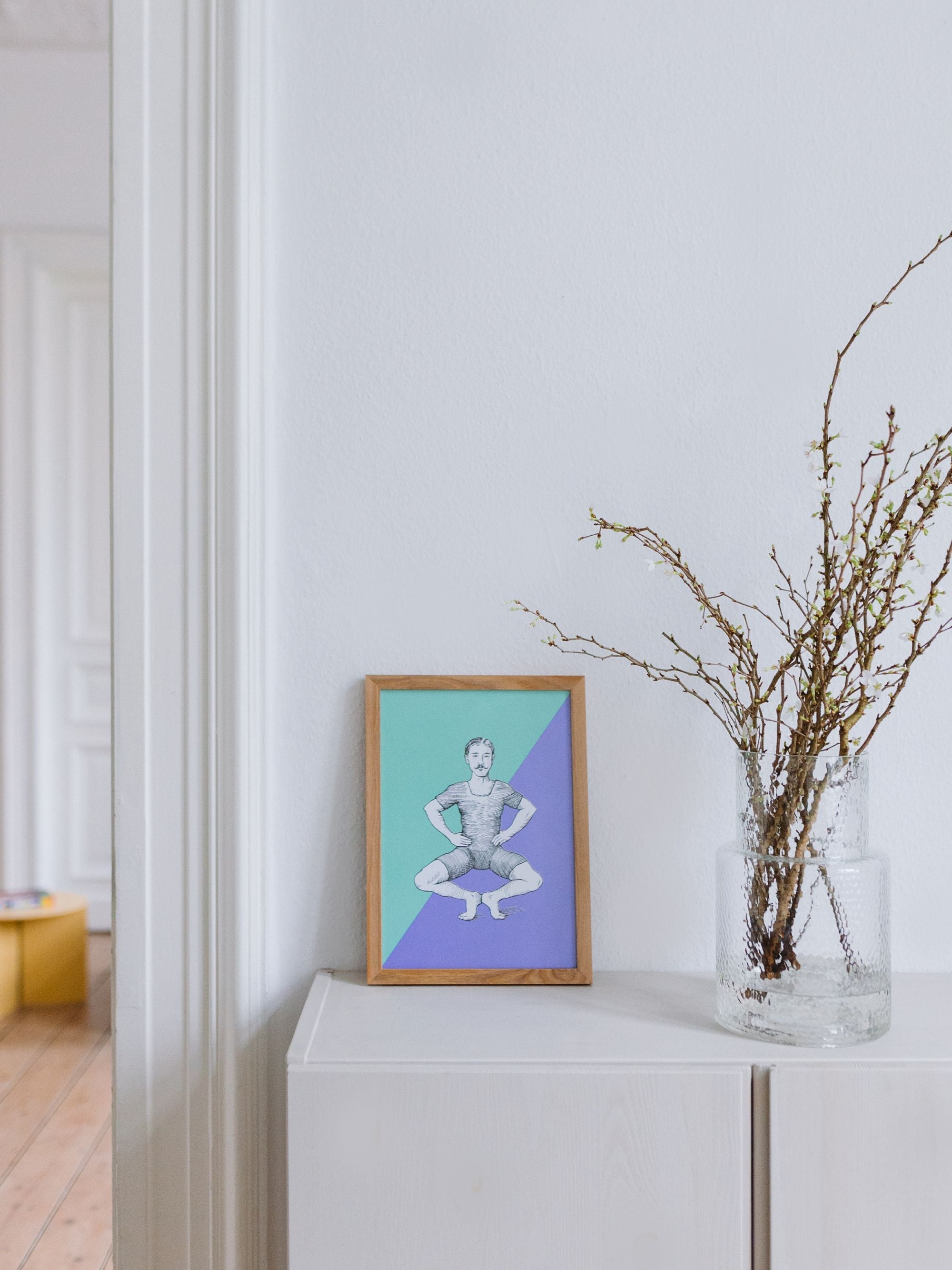 Minimalistisches Zimmer mit weißem Schrank, Vintage-Illustration eines Mannes und Glasvase mit Zweigen.
