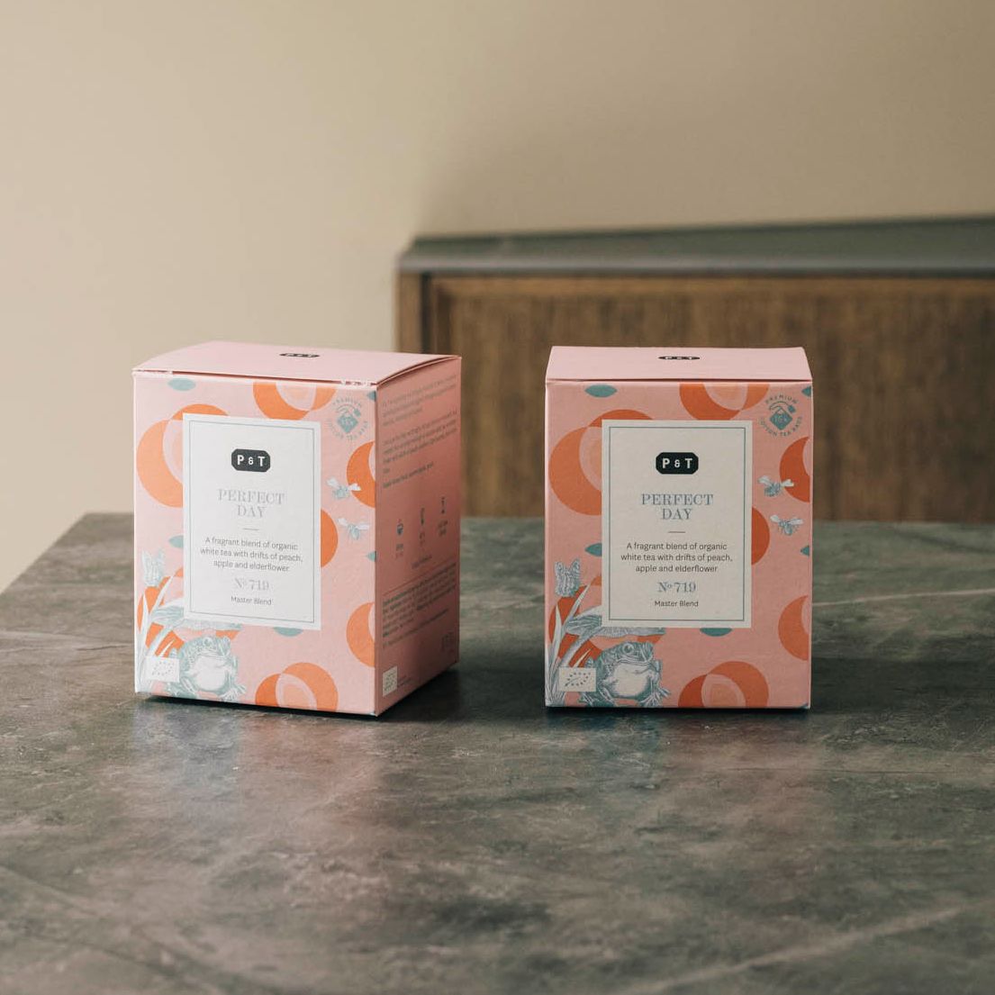 Zwei rosa Teeverpackungen mit Kreismustern und botanischen Illustrationen, Aufschrift P & T PERFECT DAY.