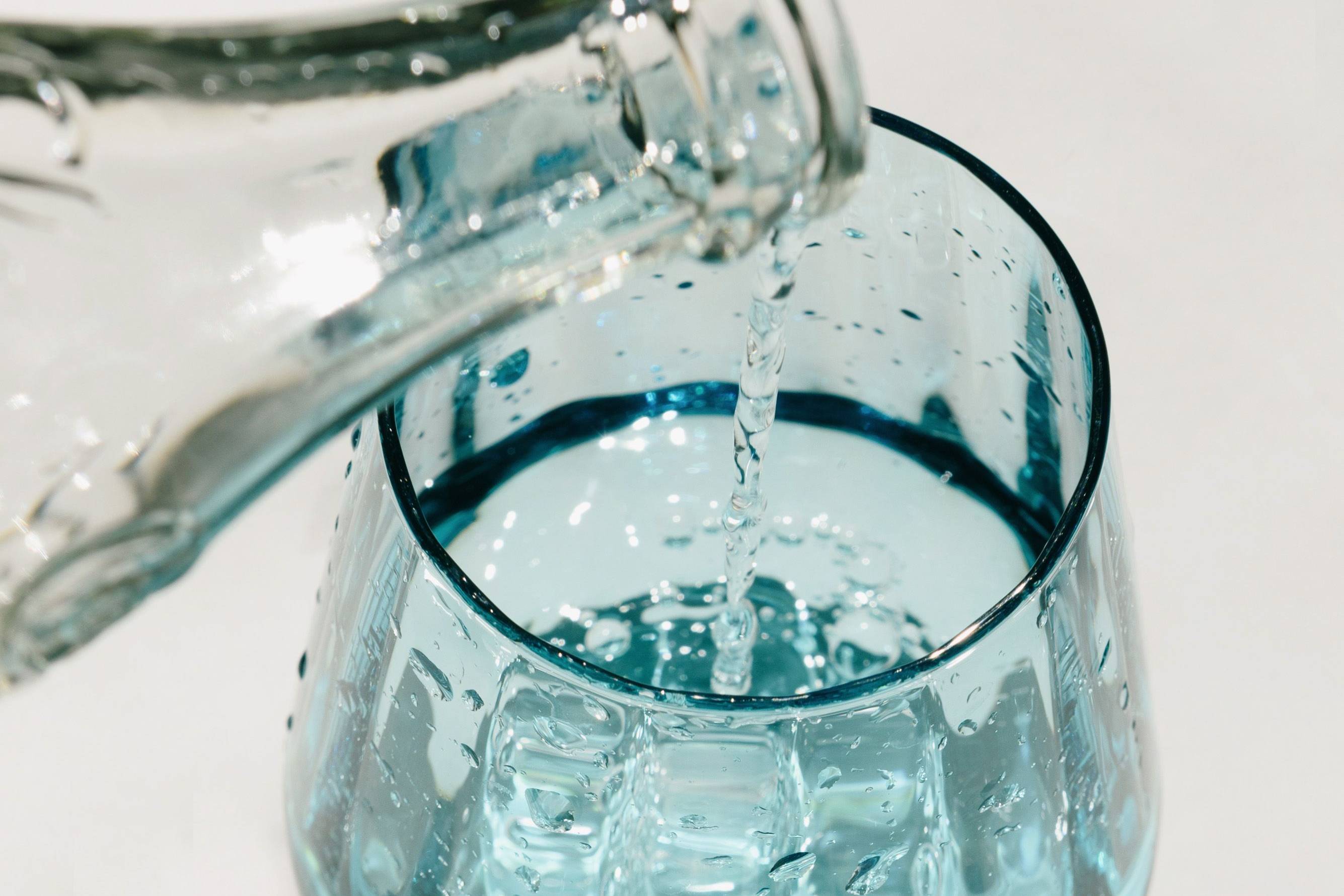 Klares Glas mit blauem Farbton wird aus einer Glaskaraffe mit Wasser gefüllt