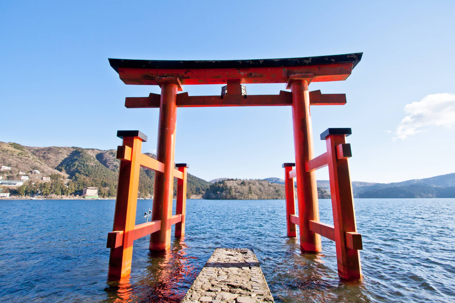 Rotes Torii-Tor in Hakone, Japan, im Wasser vor blauem See und bewaldeten Hügeln
