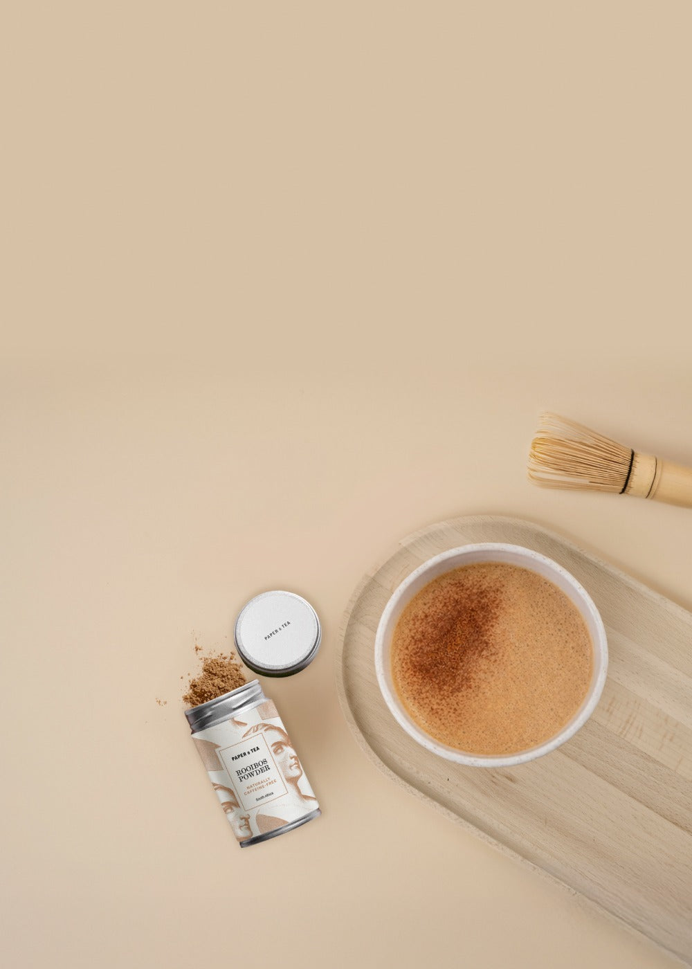 Tasse Rooibos-Tee mit Schaum und Streusel auf hellem Holztablett neben Dose mit Pulver und Bambusbesen.