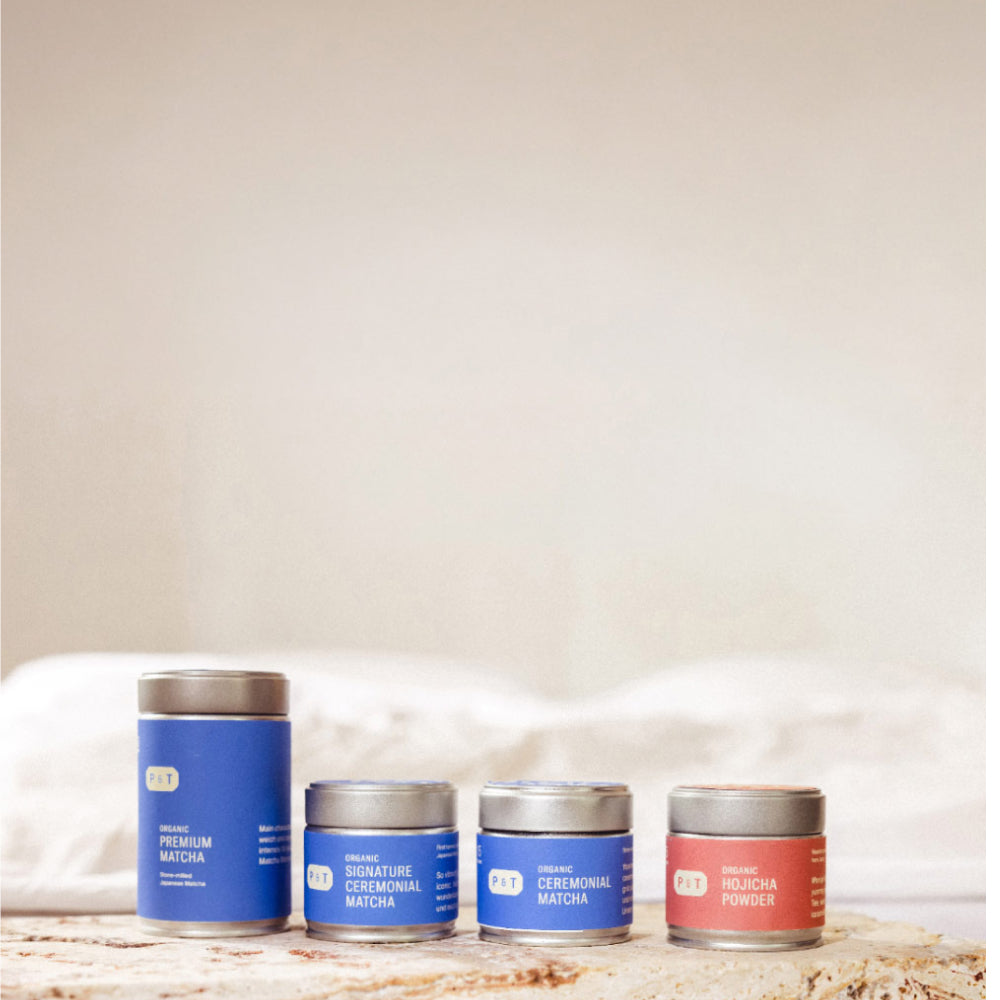Vier Metallteedosen mit silbernen Deckeln: drei blaue für P&T Bio-Matcha, eine rote für Bio-Hojicha-Pulver.