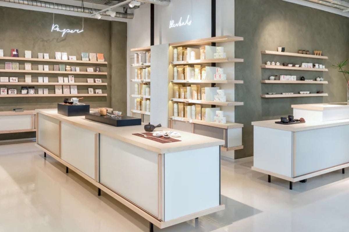 Moderner Laden mit minimalistischer Einrichtung, großem Tisch mit Teekannen und Tassen, Regale mit Zubehör.