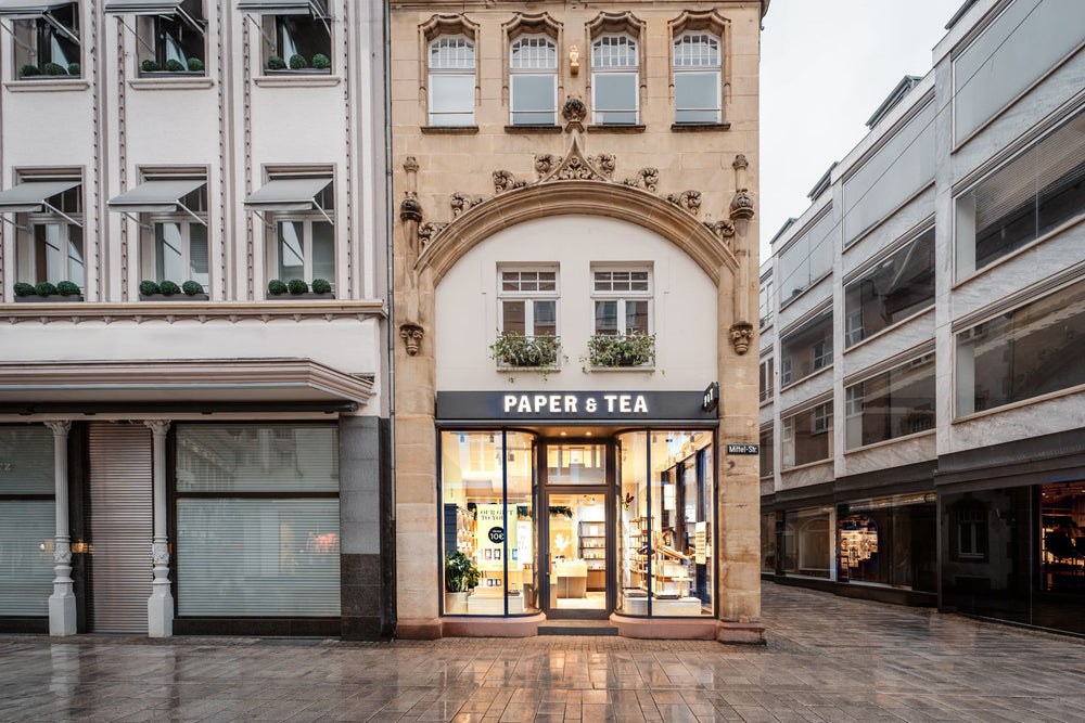 Fassade des PAPER & TEA Ladens mit großen Schaufenstern und beleuchtetem Innenraum in der Mittelstraße.