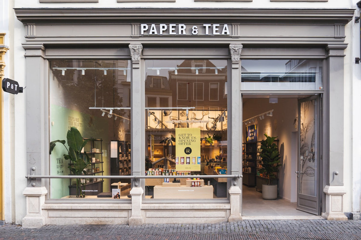 Elegantes Geschäft mit 'PAPER & TEA'-Schild, große Fenster, Teeverkostung und Eröffnungsangebot für 8 €.