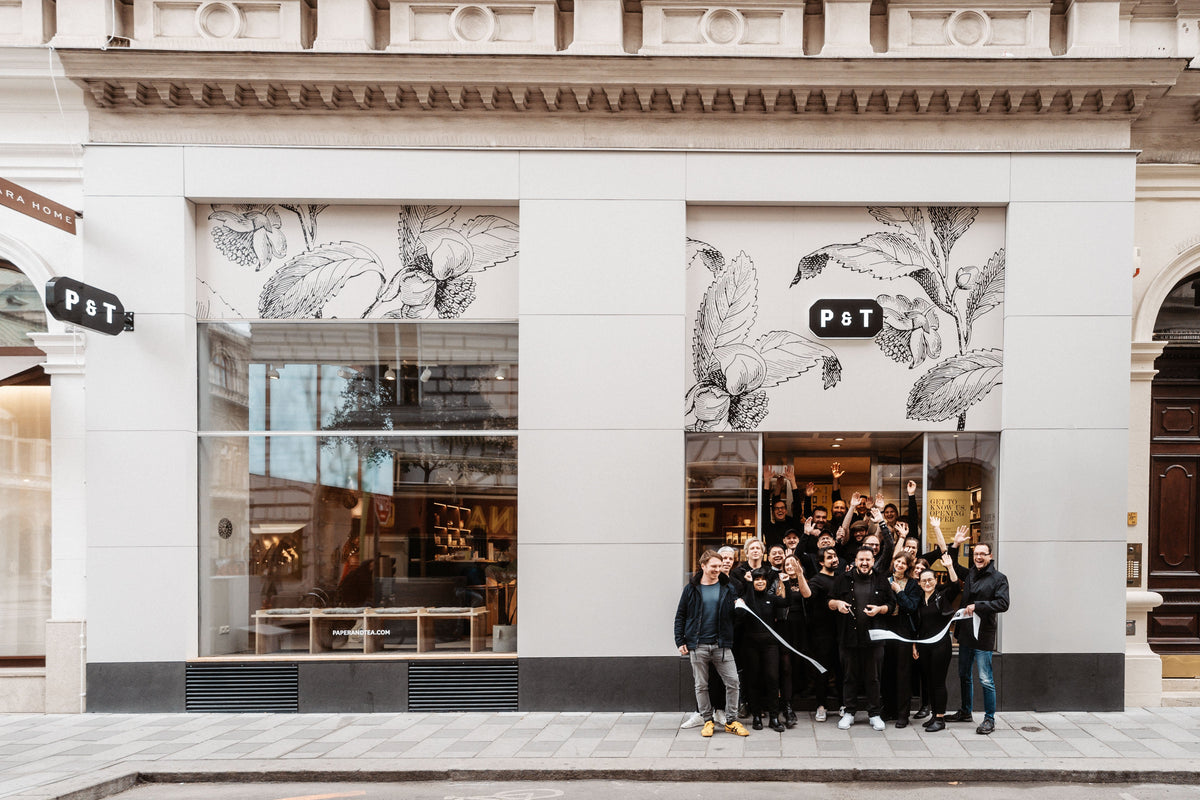 Feierliche Eröffnung des P & T Teeladens mit lachender Gruppe vor modernem Geschäft.